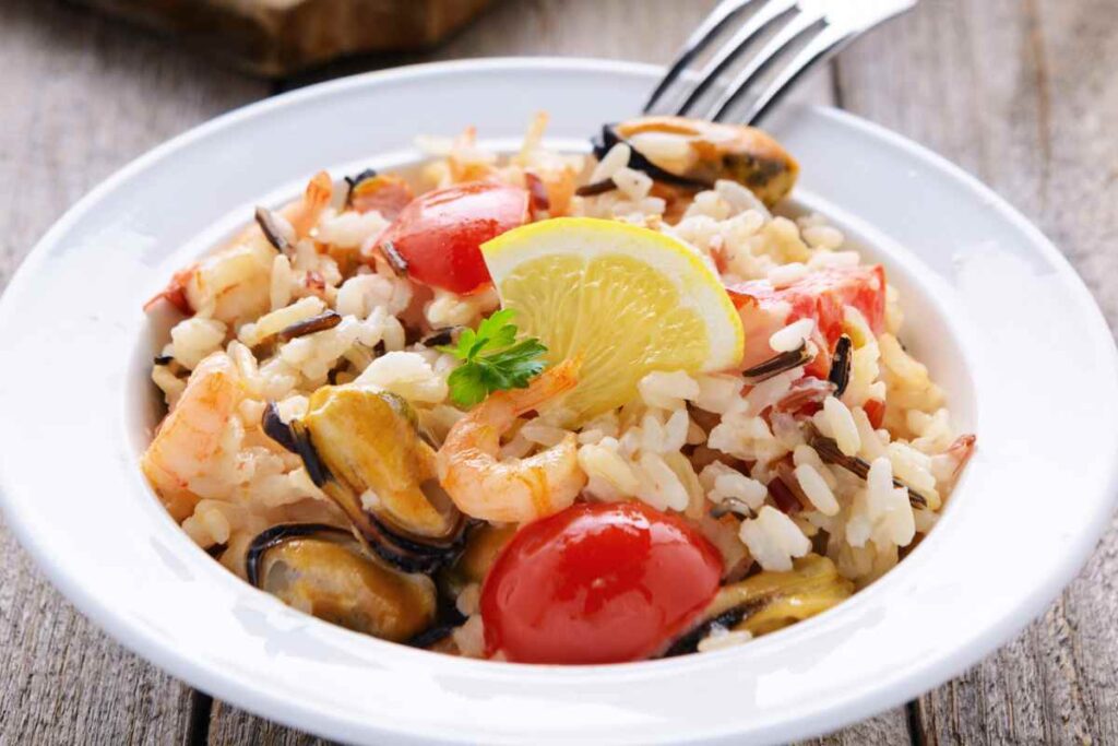 Insalata di riso alla pescatora in un piatto guarnita con spicchio di limone