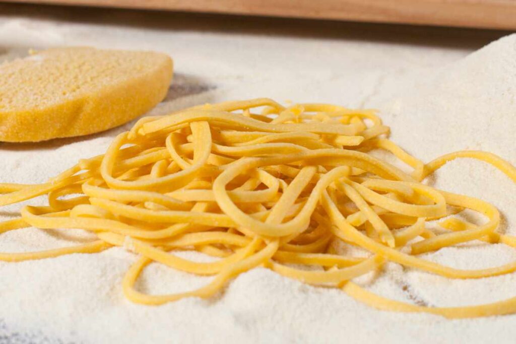 Spaghetti alla chitarra fatti in casa sparsi sul tavolo con un mucchio di semola vicino
