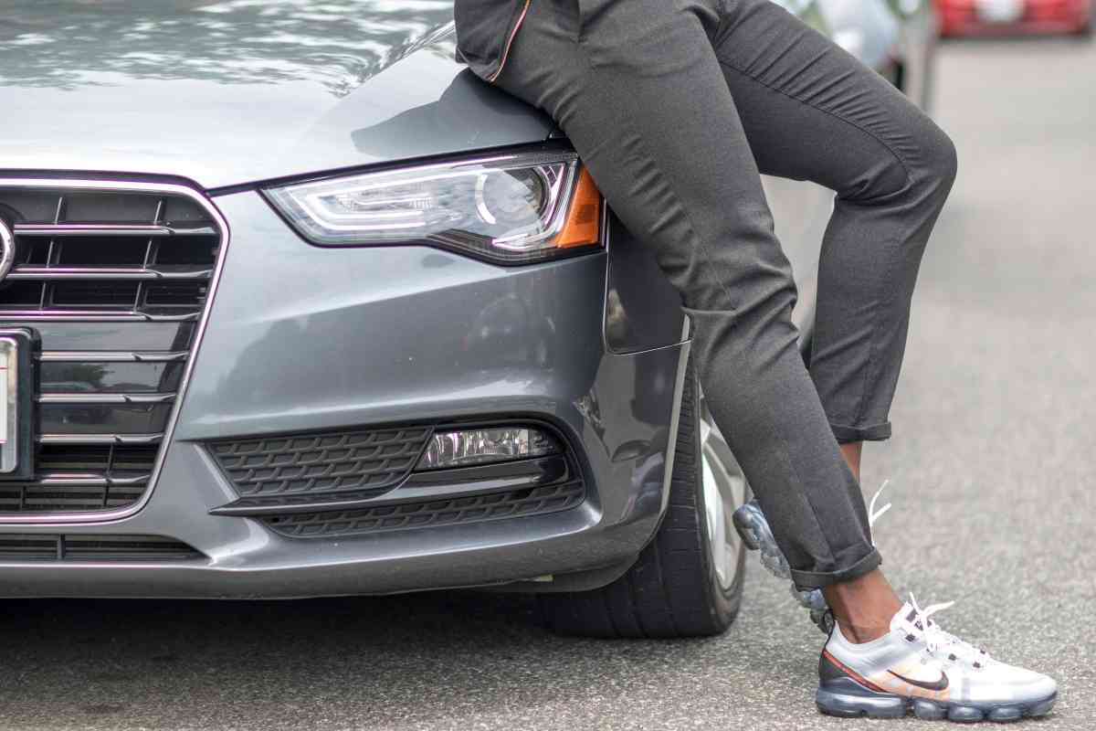 Uomo appoggiato a un'auto parcheggiata