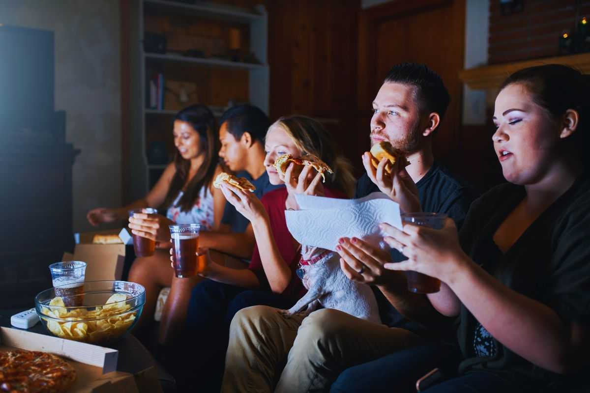 Amici che mangiano pizza sul divano mentre guardano la tv