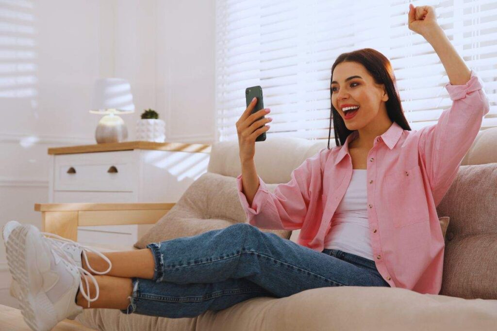 Ragazza seduta su divano che gioisce per qualcosa che vede sullo smartphone