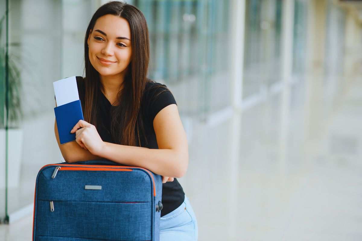 Ragazza in aeroporto con biglietto in mano e valigia