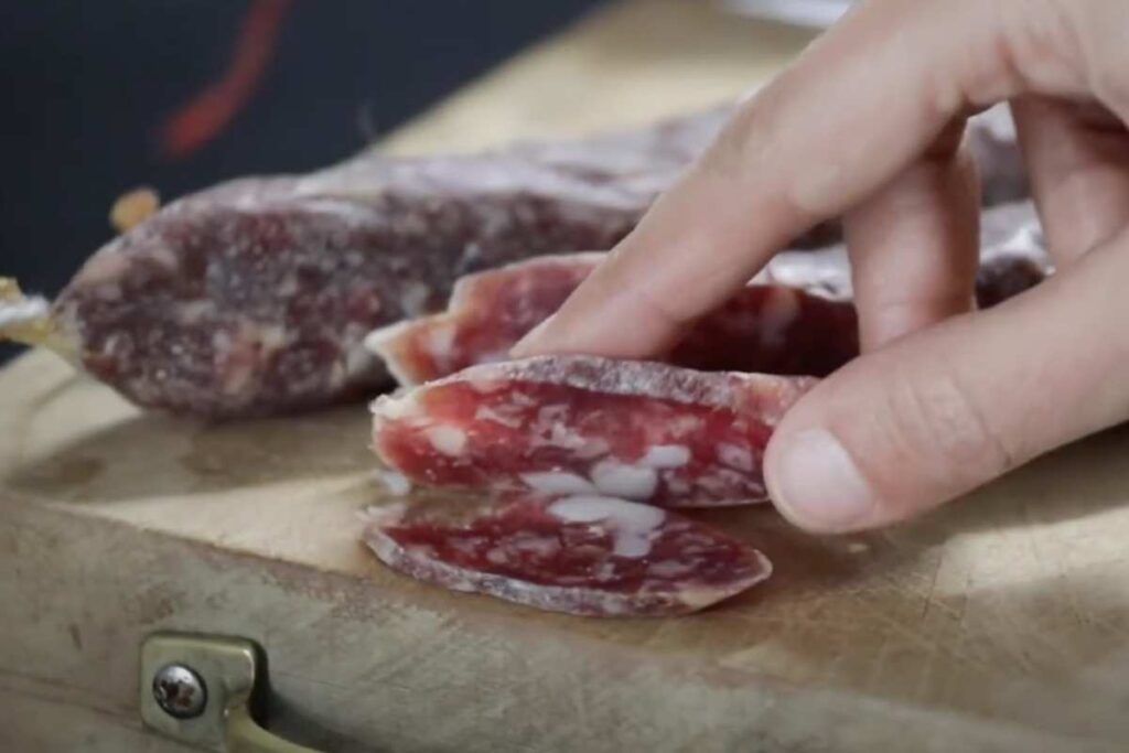 una mano e un salame tagliato a fette
