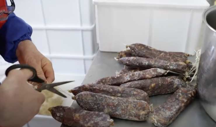 dei salami e delle mani che lavorano con le forbici