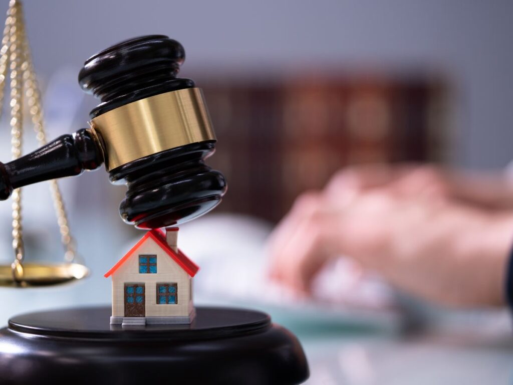 martello giudice su una casa in miniatura e sullo sfondo uomo al pc