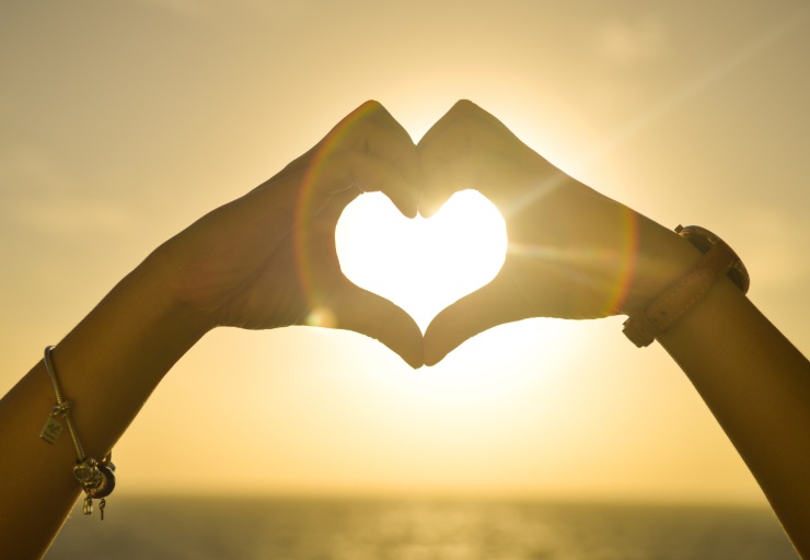 mani che formano cuore con sole all'interno