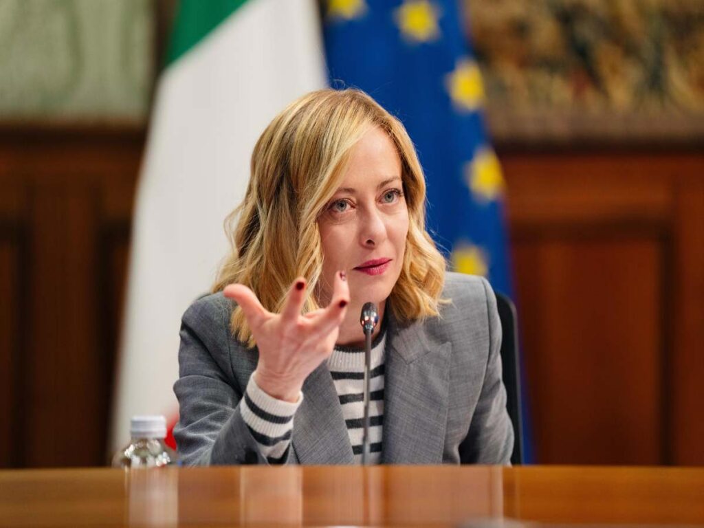 giorgia meloni seduta che parla e muove una mano