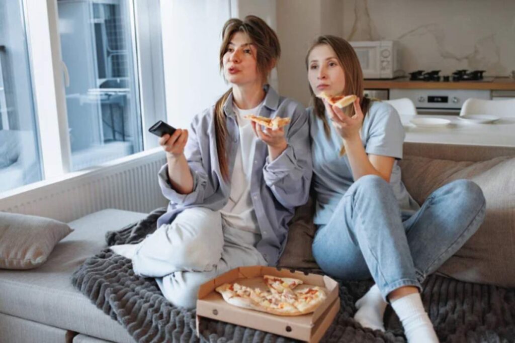 Due amiche che mangiano una pizza davanti alla tv