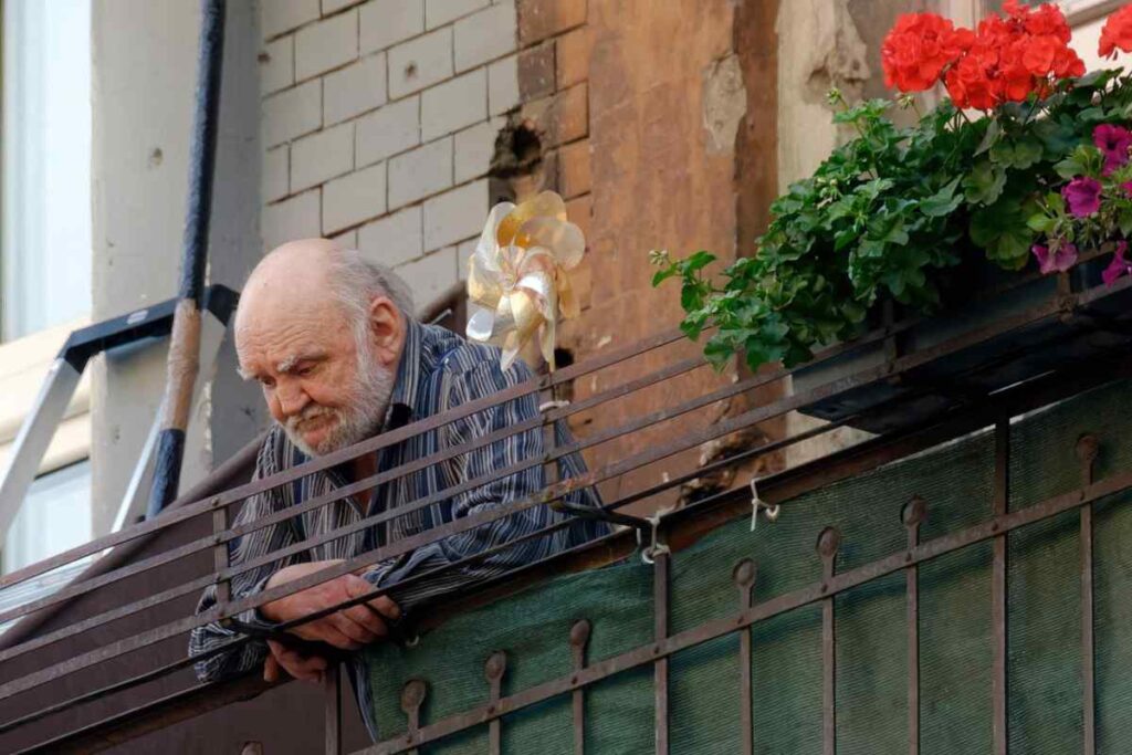 anziano con espressione triste affacciato dal balcone