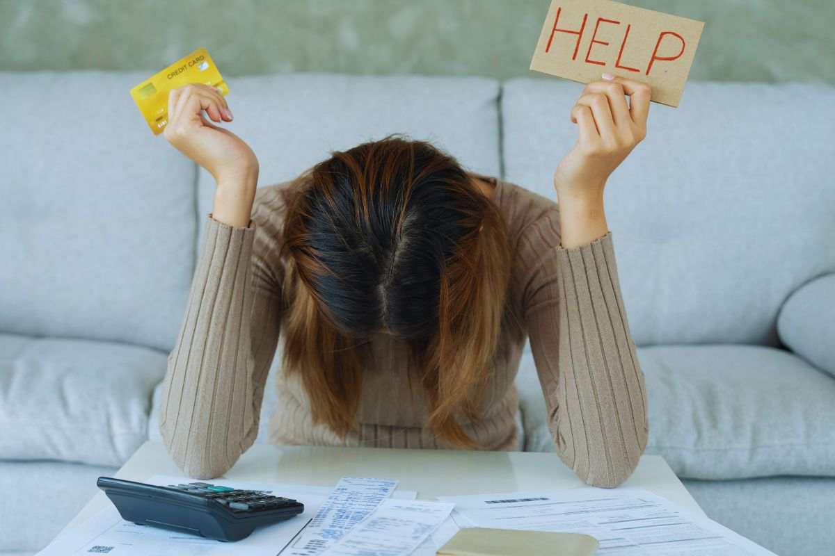 Donna sconfortata tiene in mano una carta di credito e un cartello con su scritto "Help"
