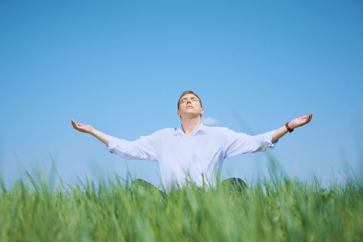 Uomo a braccia aperte su un prato rivolge il viso al sole