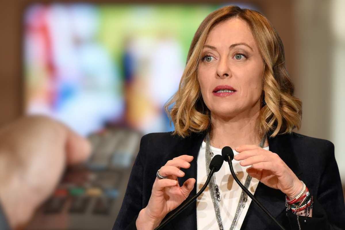 Meloni in primo piano e TV come sfondo