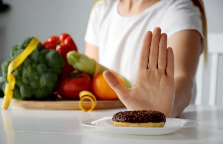 donna con frutta e verdura che dice no ad un dolce
