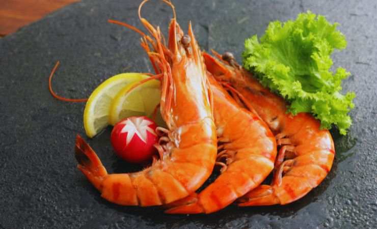 tre gamberi crudi su un tagliere, ravanello, insalata e limone