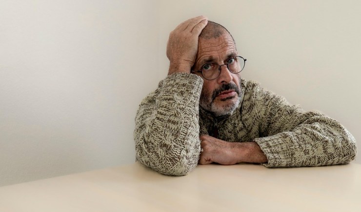 uomo seduto vicino ad una tavolo con una mano sulla testa e l'espressione disperata