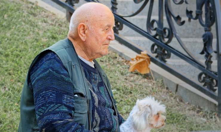 uomo anziano seduto su una panchina con accanto un cagnolino bianco