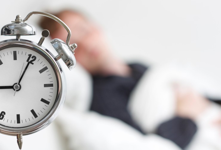 sveglia in primo piano e uomo che dorme sullo sfondo