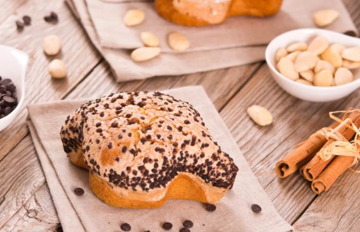colomba con gocce di cioccolato su un tavolo con accanto mandorle e cannella