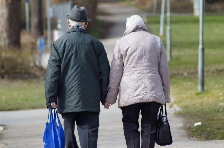 uomo e donna anziani di spalle con delle borse in mano