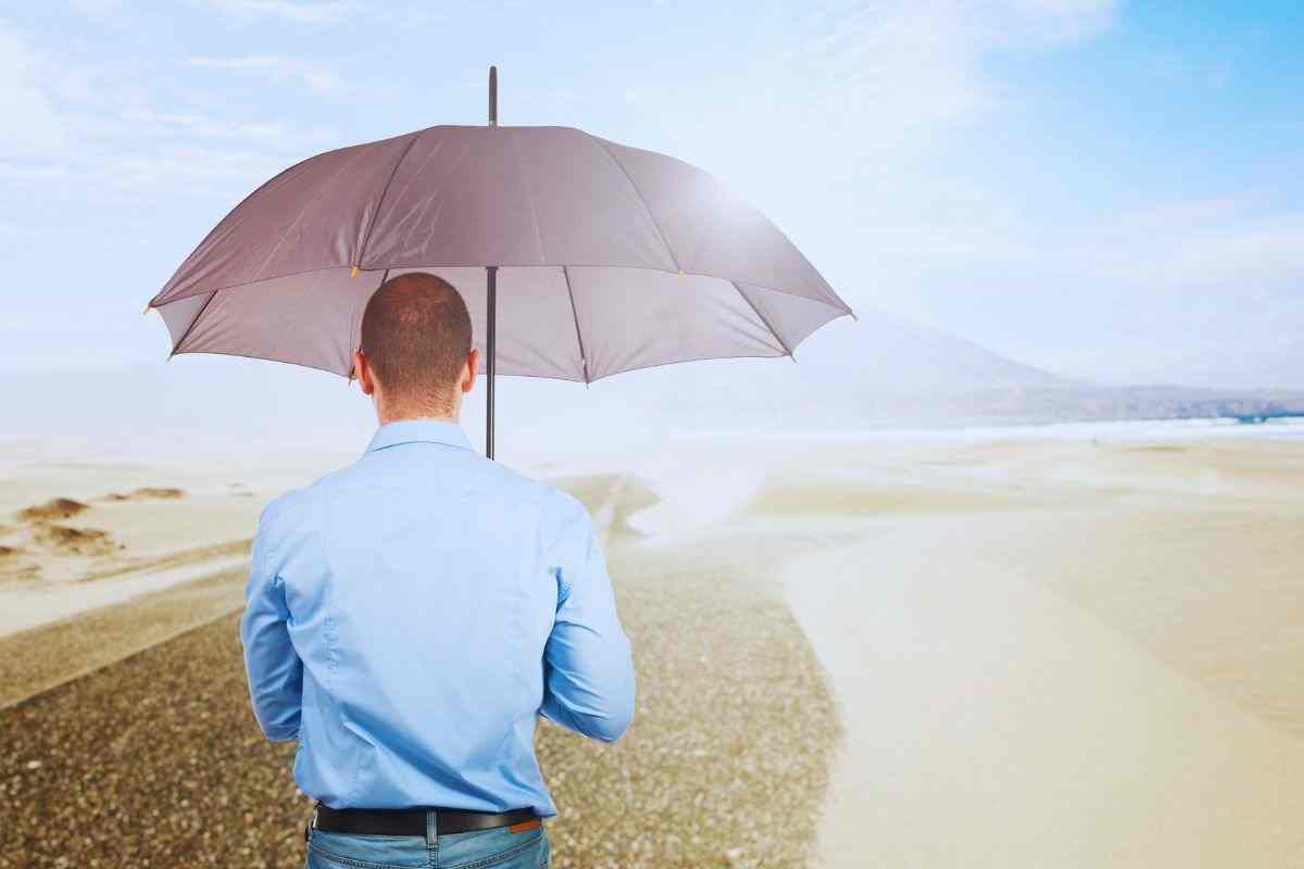 Uomo che cammina su spiaggia assolata con l'ombrello aperto