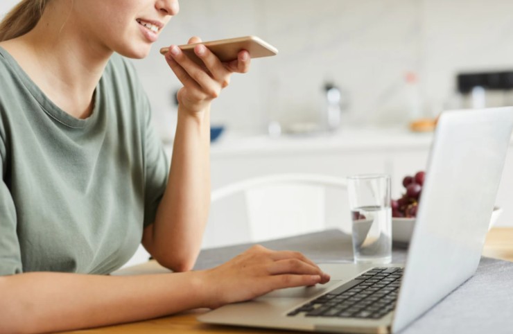 donna al pc che registra messaggio sullo smartphone