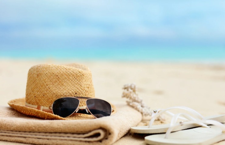 cappello occhiali da sole telo mare e infradito sopra alla sabbia