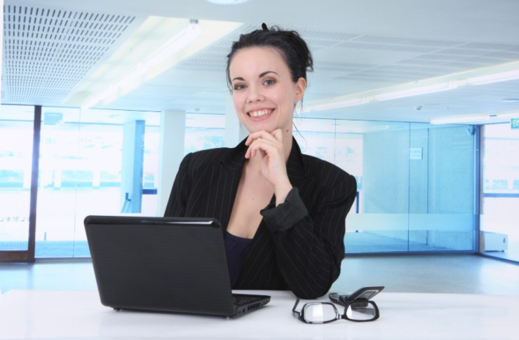 donna che sorride seduta davanti al computer con una mano sotto al mento