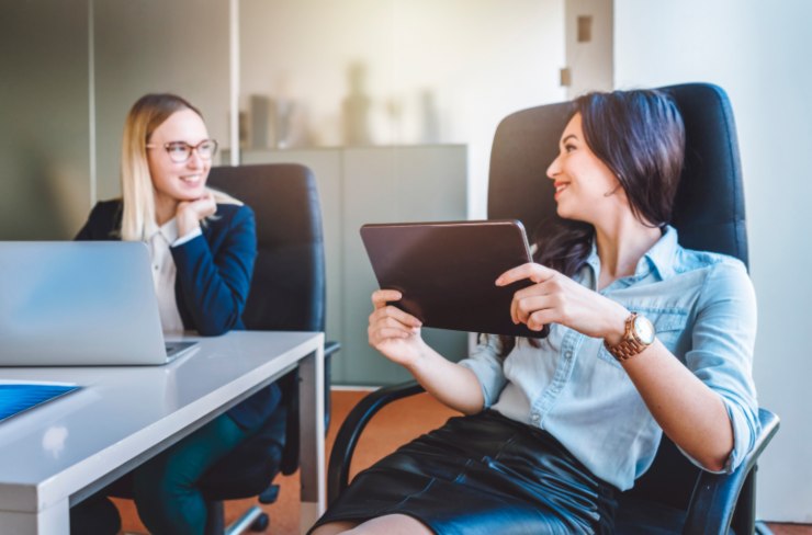 due donne in ufficio davanti al computer e al tablet che parlano e ridono