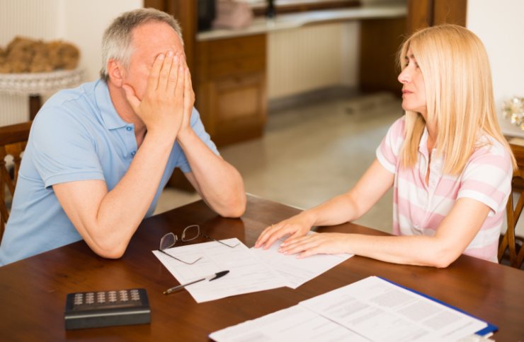 uomo e donna disperati seduti attorno ad un tavolo con davanti dei fogli e una calcolatrice