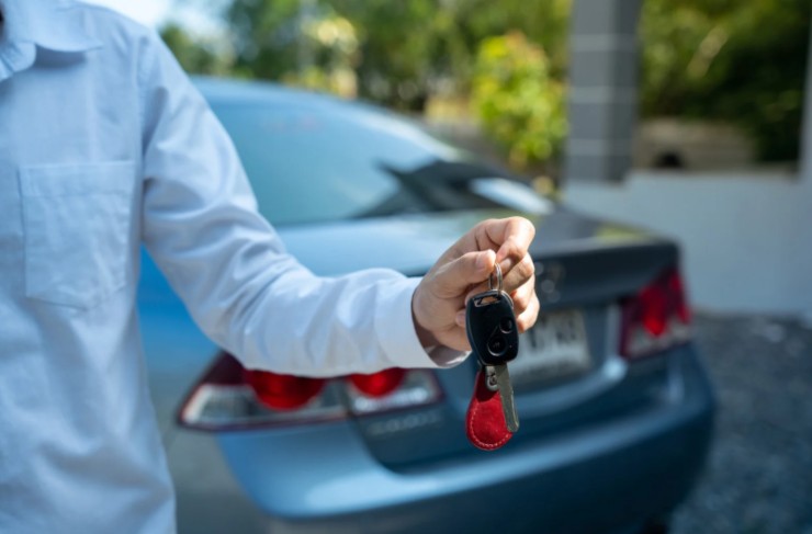 uomo con in mano le chiavi dell'auto e dietro di lui l'automobile
