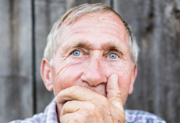 uomo anziano con una mano davanti alla bocca