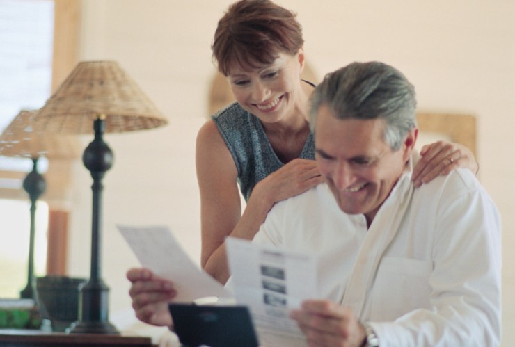 uomo seduto che guarda dei fogli e donna che sorride alle sue spalle