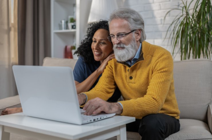 uomo e donna seduti sul divano che sorridono mentre guardano qualcosa al computer