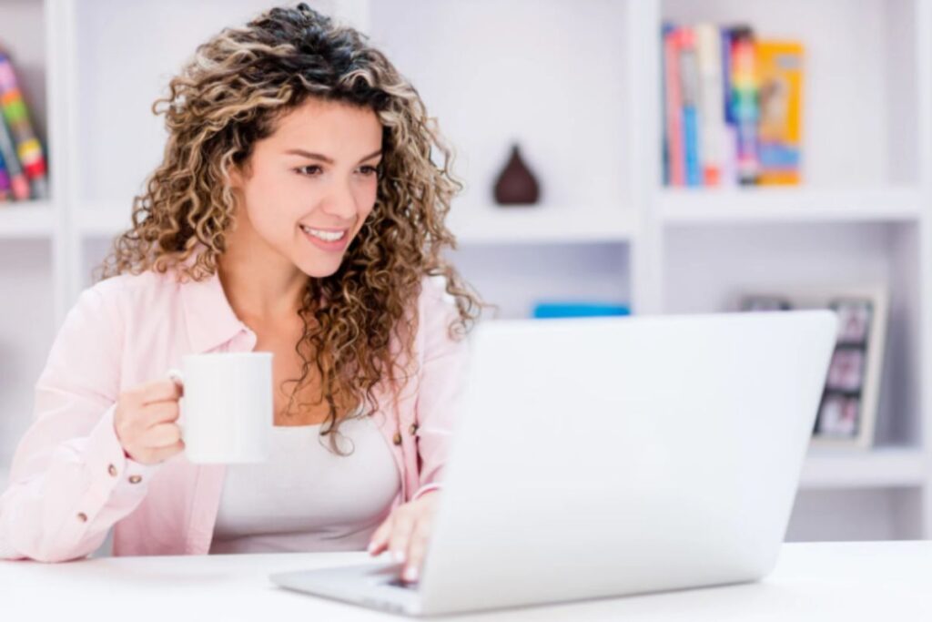 ragazza che sorride davanti al computer con una tazza in mano