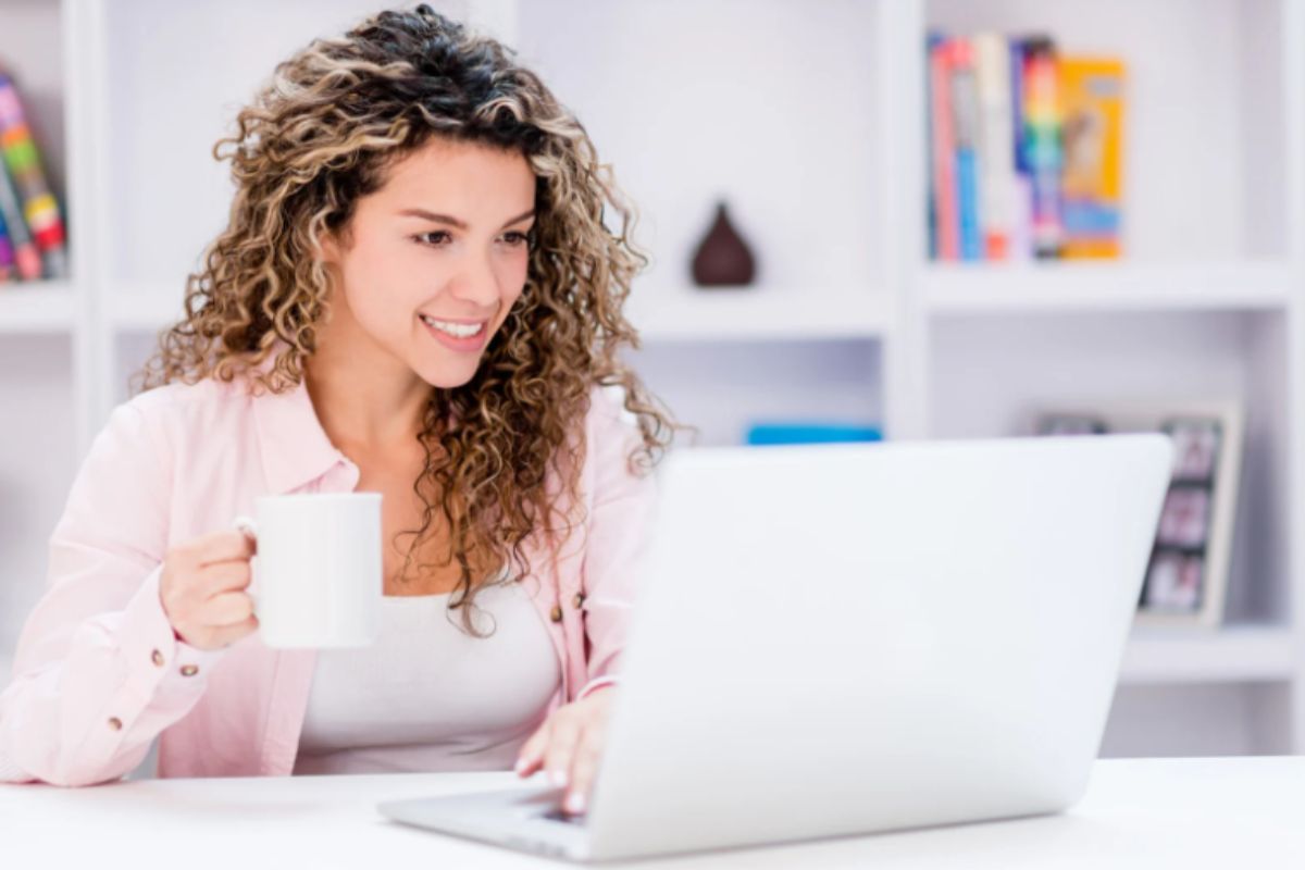 ragazza che sorride davanti al computer con una tazza in mano