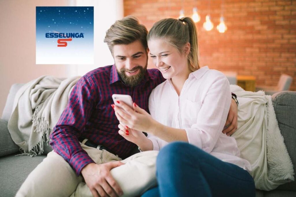 uomo e donna seduti sul divano che sorridono mentre guardano qualcosa sul cellulare