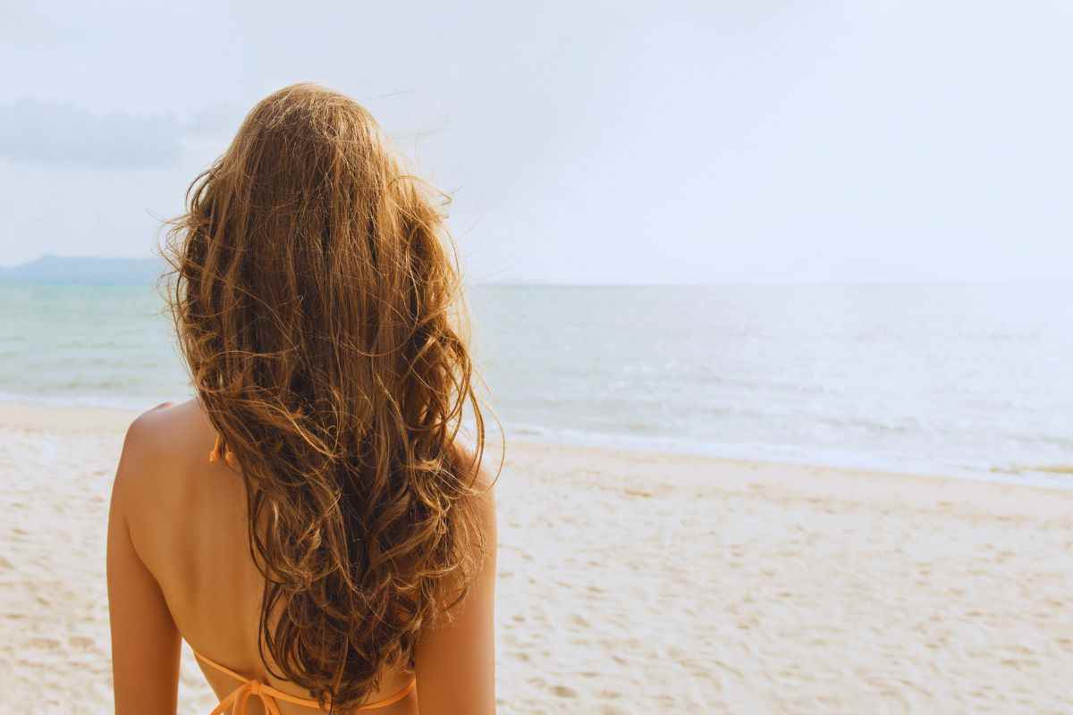 Donna sulla spiaggia di spalle che osserva il mare