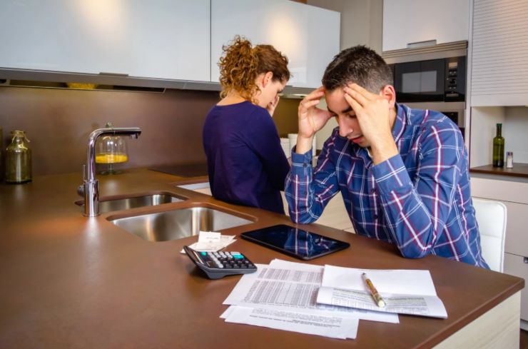 uomo e donna preoccupati con davanti dei fogli e una calcolatrice