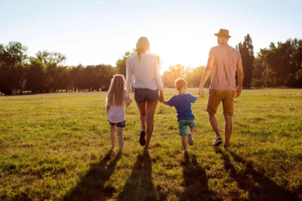 uomo e donna che tengono per mano un bambino e una bambina mentre camminano su un prato