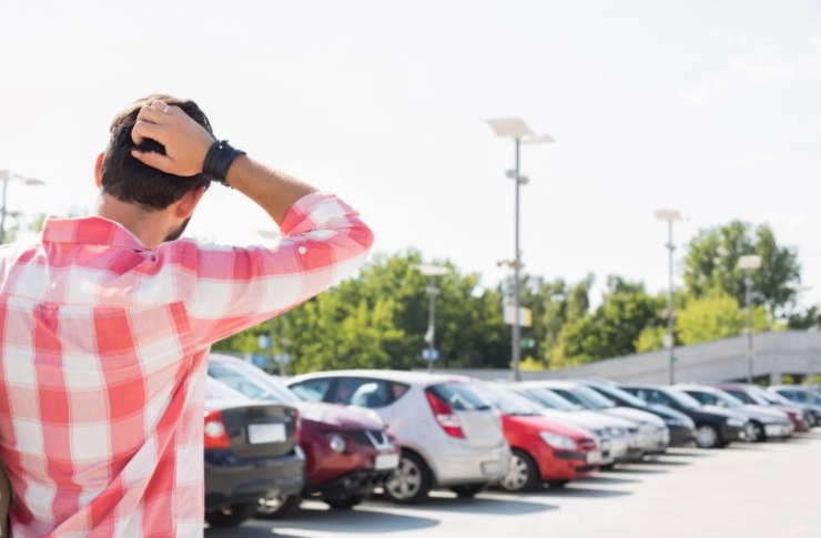 uomo che si tocca la testa in un parcheggio pieno di auto sotto al sole