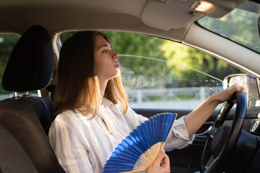 ragazza in auto che sente caldo e si soffia con ventaglio