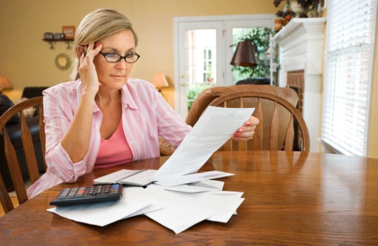 donna seduta al tavolo che legge dei fogli con accanto una calcolatrice