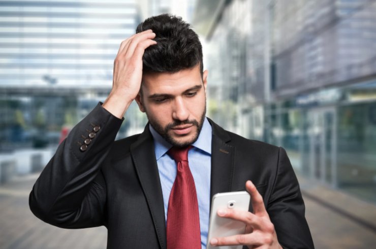 uomo perplesso che si gratta la testa con il cellulare in mano