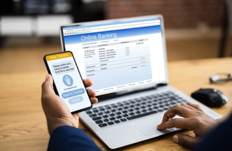 uomo davanti al computer a con il cellulare in mano che fa un bonifico