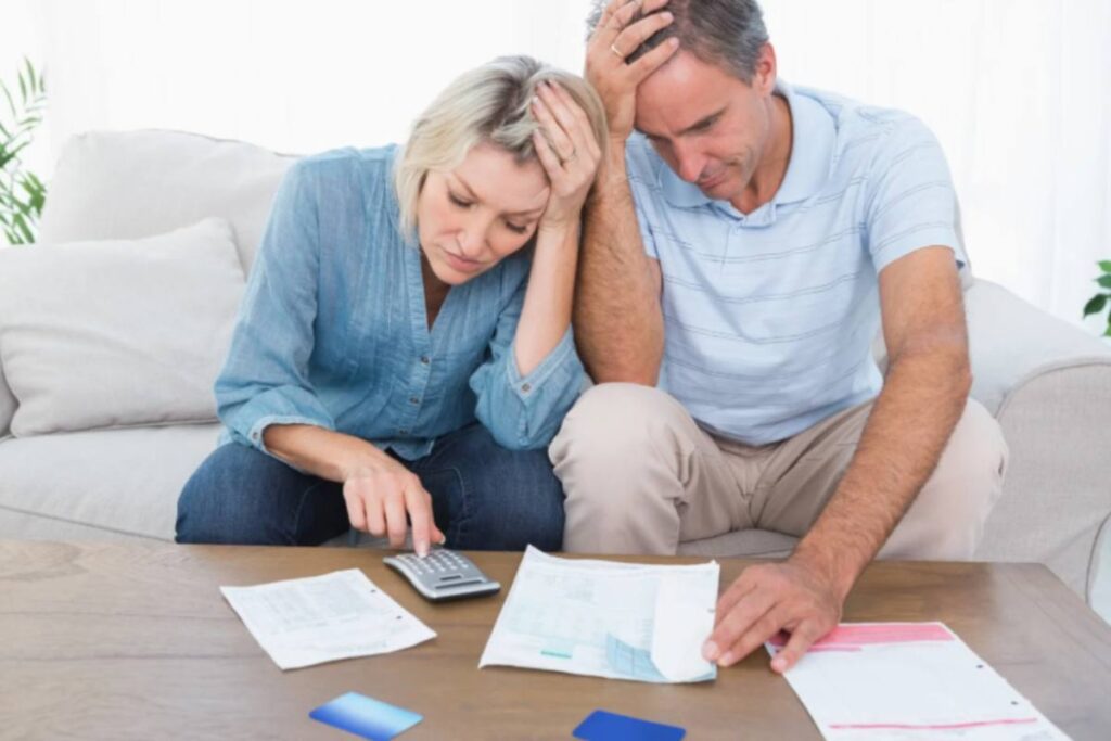 uomo e donna disperati seduti sul divano che fanno i conti con la calcolatrice