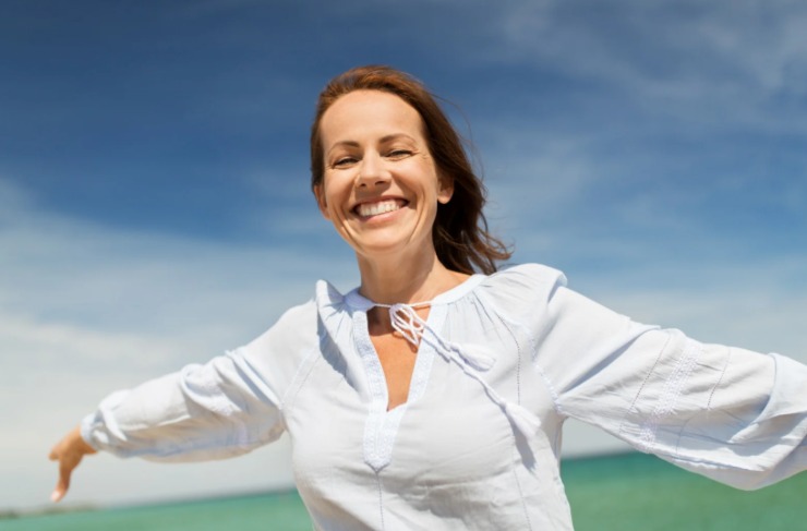 donna che sorride e allarga le braccia in spiaggia