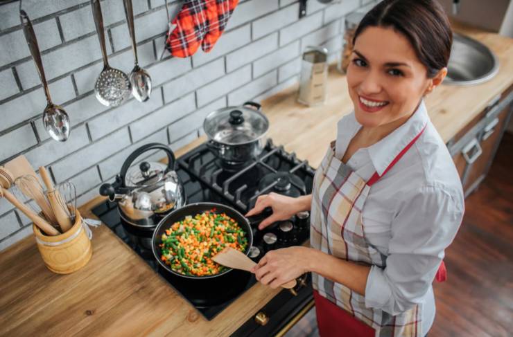 donna che sorride mentre cucina delle verdure in padella