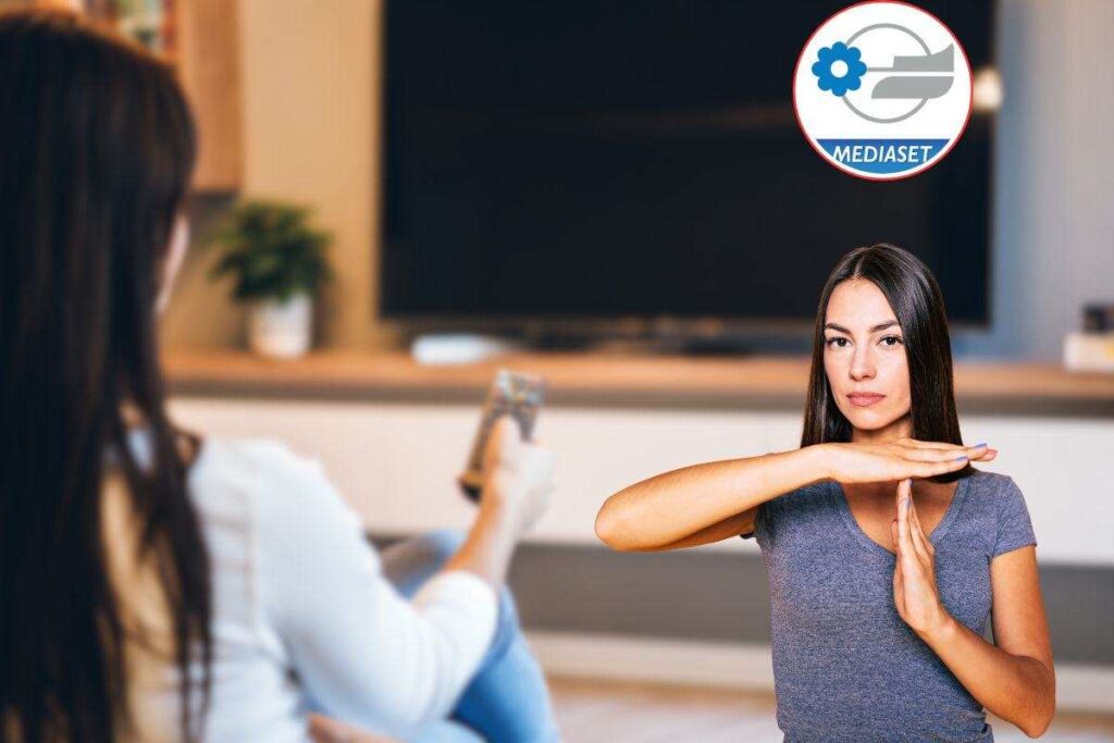 donna che guarda tv, logo mediaset e un'altra donna che fa stop con le mani