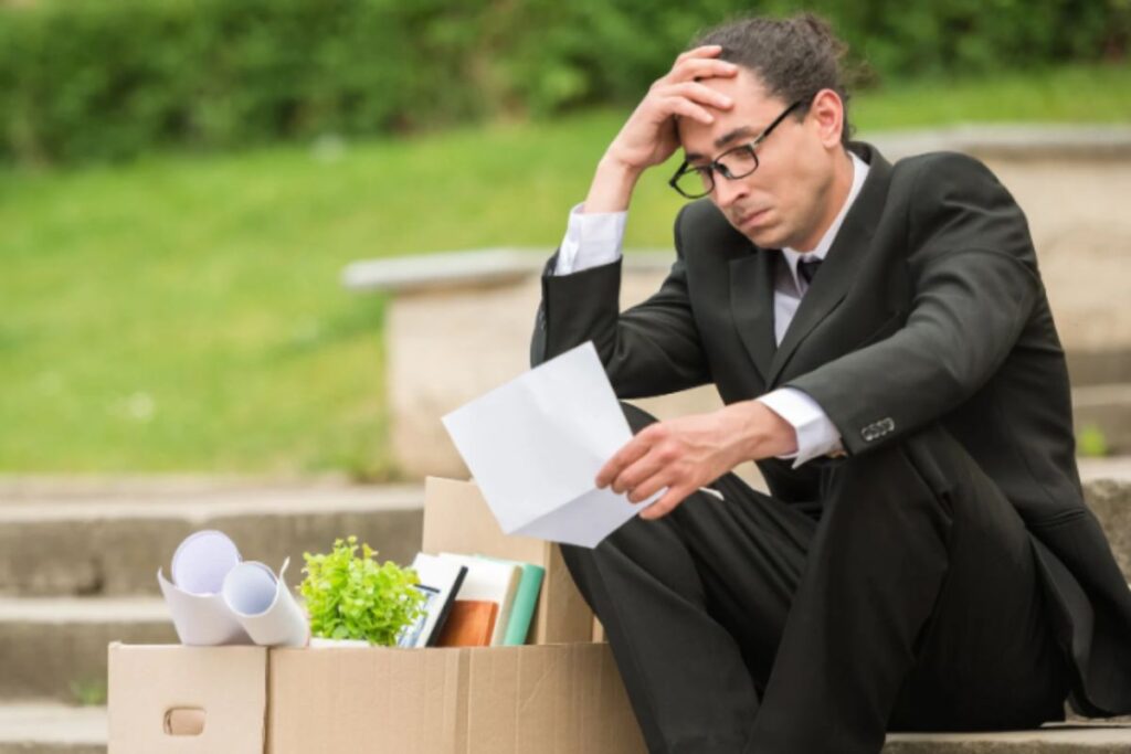 uomo disperato seduto sulle scale che legge un foglio con accanto uno scatolone