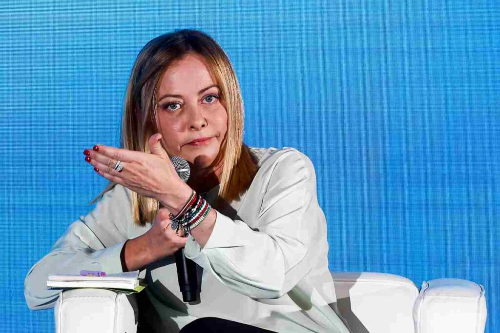 il premier giorgia meloni seduta e con un microfono in mano